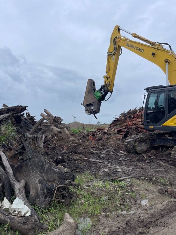 30-tonne excavator with timber shears preparing green waste for processing on a land clearing site.