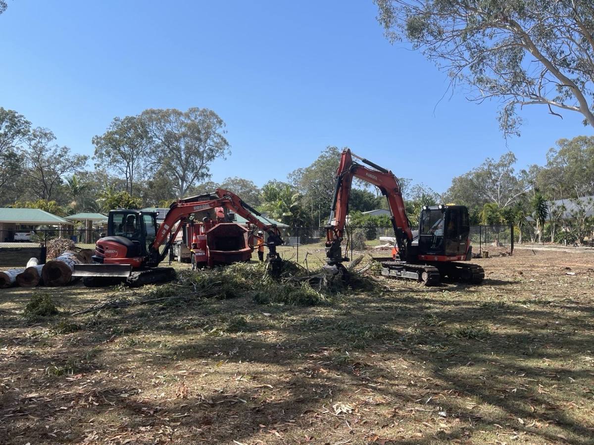 Two excavators with grabs stacking cleared trees on a block, Brisbane