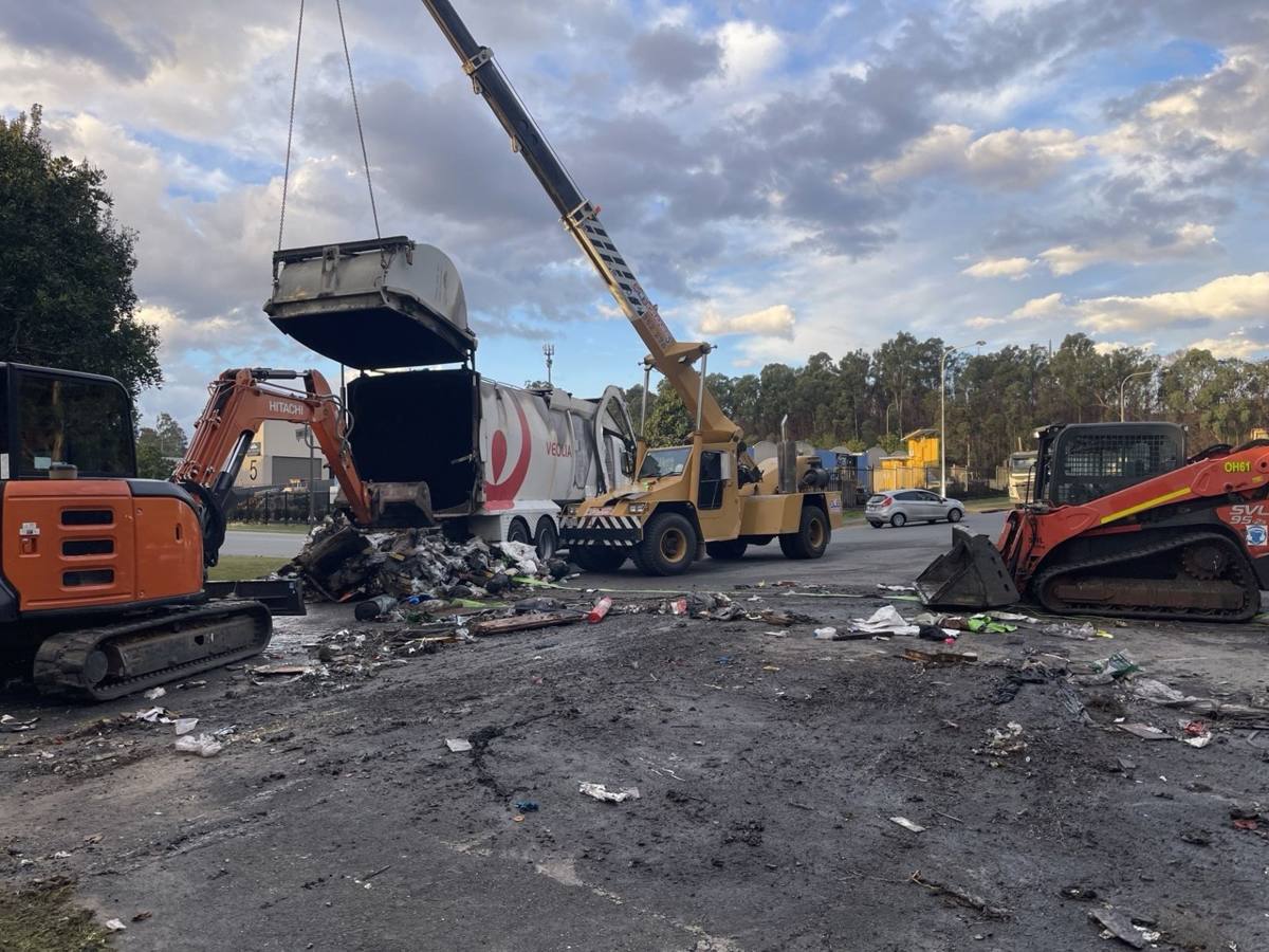 Crane lifting a bin with an excavator and skid steer on a storm clean-up site